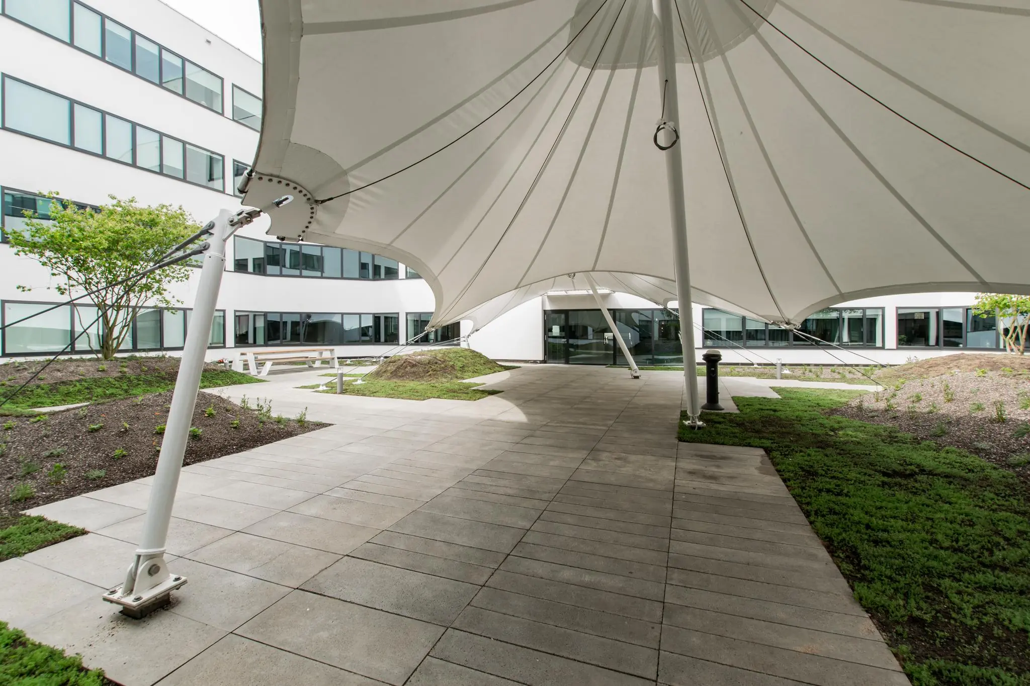 Overdekte binnenplaats met witte luifel, bestrating, groene perkjes en moderne kantoorgebouwen aan de Grote Marktstraat.